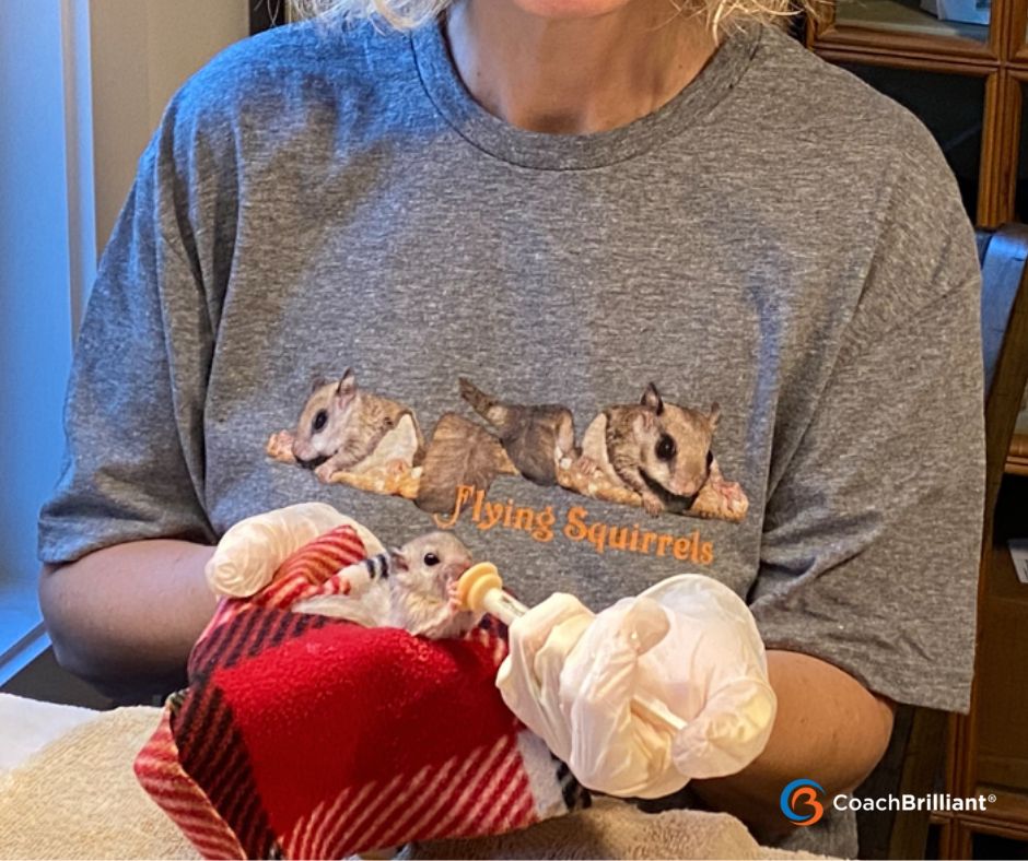 Elaine hand-feeds a tiny orphaned flying squirrel, illustrating presence and slowing down — the lesson behind how coaches get in their own way.